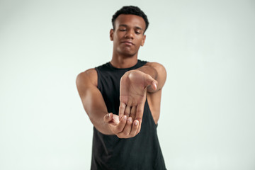 Naklejka na ściany i meble Flexible body. Strong young afro american man stretching his arms while standing against grey background