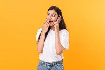 Image of pleased brunette woman wearing basic clothes rejoicing while talking on cellphone