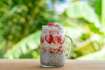 Almond milk chia pudding with fresh red strawberries, goji berries and oat flakes in a glass jar mug. Vegan raw breakfast. Chia seeds and fresh cut fruits and berries dessert