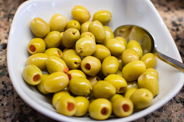 White ceramic bowl filled with pitted green olives, stuffed with marinated red pepper. Olives from Turkey.
