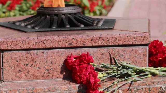 Monumen with star and flowers at Grave of Unknown Soldier. Carnation red flowers on granitic steps by Eternal flame monument. Fire burns in memory of millions fallen people defenders motherland.