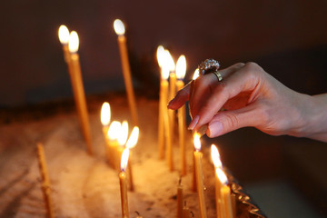 A female hand lights a candle in a church. The concept of faith in God. Photo without a face.