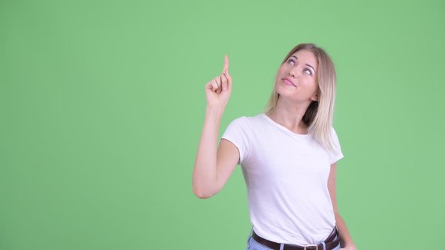 Happy young beautiful blonde woman thinking and pointing up