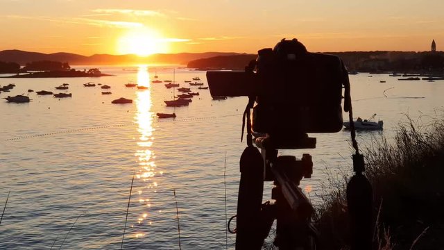 Making timelaps with professional camera at sunrise. Shooting landscape timelaps with boats in marina bay, sea, colorful sky in golden hours.