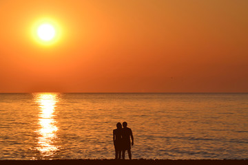 Obraz premium Silhouettes of romantic hugging couple on the beach at sunrise