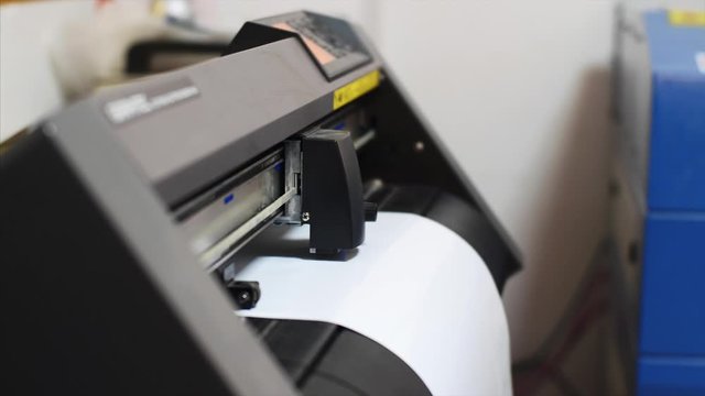 Industrial modern computerized equipment in printing house. Plotter machine cutting self-adhesive film and stickers in printing office, side view. Publishing business and industry.