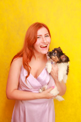Fototapeta na wymiar Relaxed red-haired girl embracing puppy on yellow background. Studio portrait of white appealing woman chilling with dog.