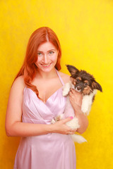 Obraz premium Relaxed red-haired girl embracing puppy on yellow background. Studio portrait of white appealing woman chilling with dog.