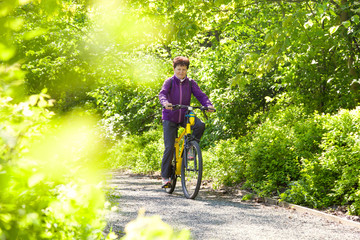 Happy beautiful senior woman riding a bike in summer park
