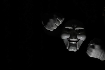 White scary mask on a black background with whites hand.