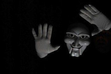 White scary mask on a black background with whites hand.