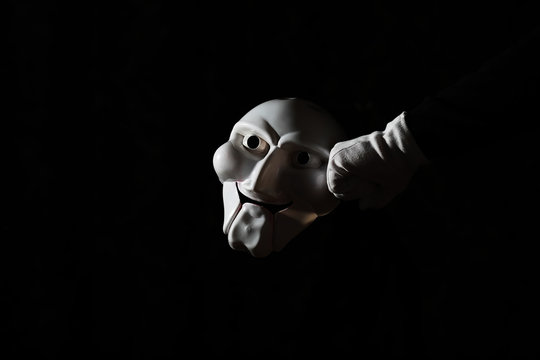White scary mask on a black background with whites hand.