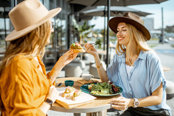 Two female best friends eating healthy food while sitting together on a restaurant terrace on a...