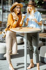 Two female best friends spending time together on the cafe terrace, feeling happy standing with...