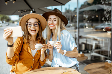 Two female best friends making selfie portrait while spending time together on the cafe terrace during a summer day