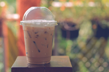 Side view Ice coffee (cappuccino, latte, mocha) in plastic cup with water drop on wooden column with blurry garden background with copy space for your text. Vintage tone
