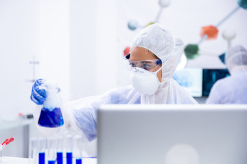 Researcher looks at a blue liquid container in front of a laptop