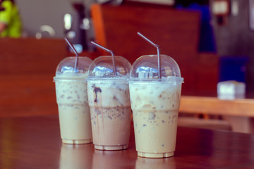 Side view Ice coffee (cappuccino, latte, mocha) in plastic cup and brown straw with water drop on wooden table with blurry cafe background with copy space for your text. Vintage tone.
