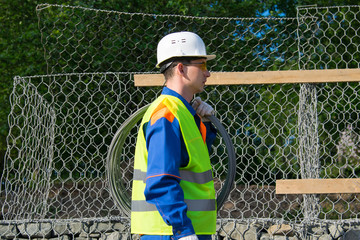 a worker in a white helmet, against the background of the grid, carries a wire on his shoulder