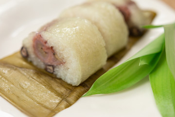 Thai dessert sticky rice or Khao Tom Mad, Wrapped the banana in sweet sticky rice on the white plate with sackcloth background.
