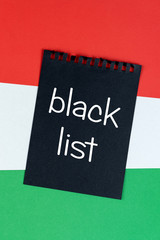 Blacklist Hungary. Mourning, ban, sanctions, politics. black sheet of notepad is on Hungarian flag. Mock up, copy space, pattern, cardboard texture.