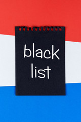 Blacklist Holland. Mourning, ban, sanctions, politics. black sheet of notebook lies on holland flag. Mock up, copy space, pattern, cardboard texture.