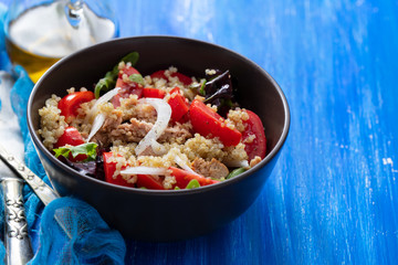 salad quinoa with tuna, tomato and lettuce in brown bowl on blue wooden background