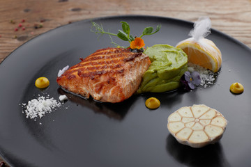 Piece of the fried salmon on a black dish with a lemon. steak. Filet