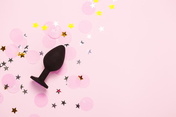 Adult sexy toy anal plug on pink background with confetti. Top view, flat lay.