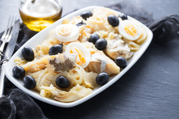 cod fish with onion, olives, eggs and olive oil on dish on ceramic background