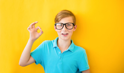 Handsome teen boy showing OK sign on a yellow background. Ophthalmic positive concept
