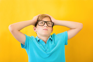 Frustrated boy holding his head on a yellow background. Study, difficulties and problems concept