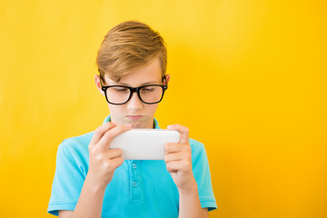 Handsome boy in glasses plays tablet on yellow background.. The concept of poor eyesight, harm of...