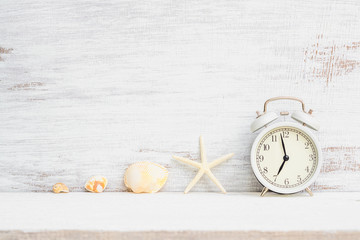 White alarm clock with starfish, sea shells on white rusty wood background. Background concept for Summer time holiday vacation, Sea beach travel vacation  time.