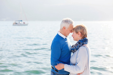 Fototapeta na wymiar Cute senior couple is hugging and embracing at sea beach outdoor. Happy elderly man and woman enjoying retirement and life. Concept of wellbeing, happiness, male and female health, tenderness.