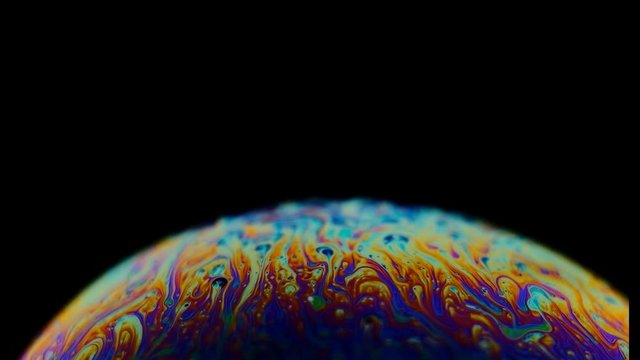 Multicolored rainbow colors of a single soap bubble that looks like a fantasy planet isolated against a black background