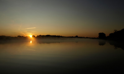 sunrise above a river on foggy summer morning, the sky reflections in the water,  misty reflection in steaming water, Salaca river, Latvia 