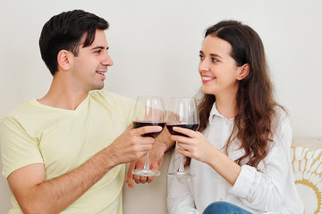 Smiling boyfriend and girlfriend toasting with wine glasses and looking at each other when having date at home