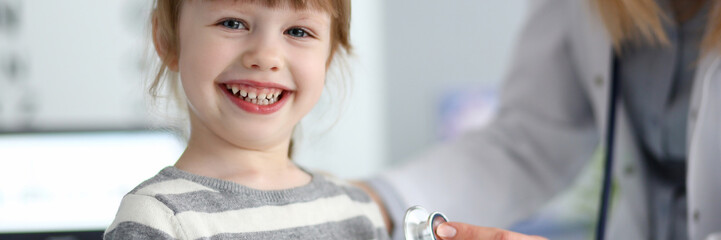 Smiling cute little girl with doctor measuring heart beat with stethoscope portrait