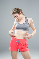 Close up of fit woman's torso with her hands on hips. Female with perfect abdomen muscles on grey background