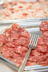 Metal tray of ready-sliced salami with a fork