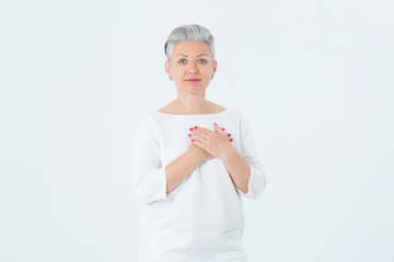Beautiful mature woman in love. Female with gray hair holding herself heart two hands, with enjoying smiling face. Positive emotion.