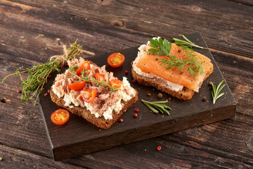 Sandwiches with salmon and tuna and butter on bread on a cutting board on a wooden table