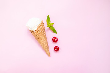 Mint vanilla ice cream with in a waffle cone with mint leaves and ripe cherry berries on a pink plain background.