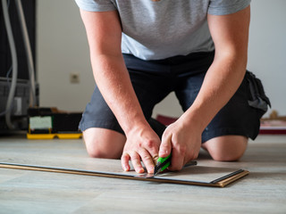 Junger Mann mit Messer in der Hand beim Bodenverlegen, Handwerker