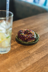 Cold lemonade with ice and lemons in a tall glass with a disposable tube. Chocolate donut with dressing.