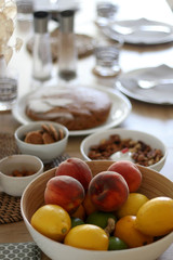 Bowl of fruit (peach, lemon, lime) served on a table, with desserts and nuts in the background. Selective focus.