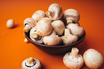 Mushrooms in a wooden bowl on an orange background. The small white champignon in a plate and scattered near it.