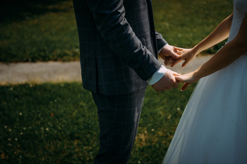 Wedding theme, holding hands newlyweds on green grass background. Hands of the bride and groom close-up. A couple on their wedding day, a touching moment.