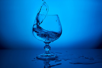 Water splash and waves in glass on blue lighting reflective background with drops.